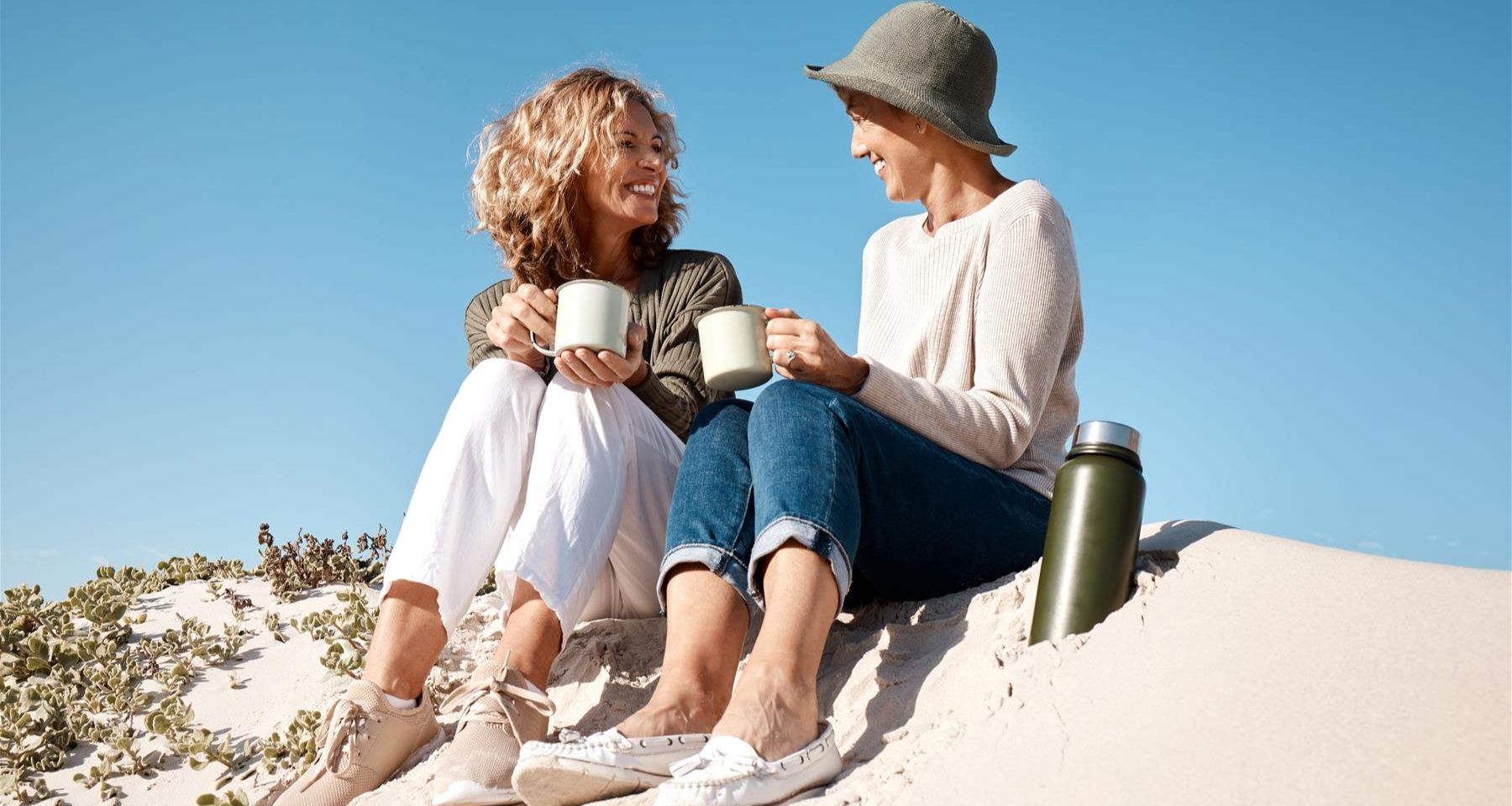 Two women sitting on a sand dune.